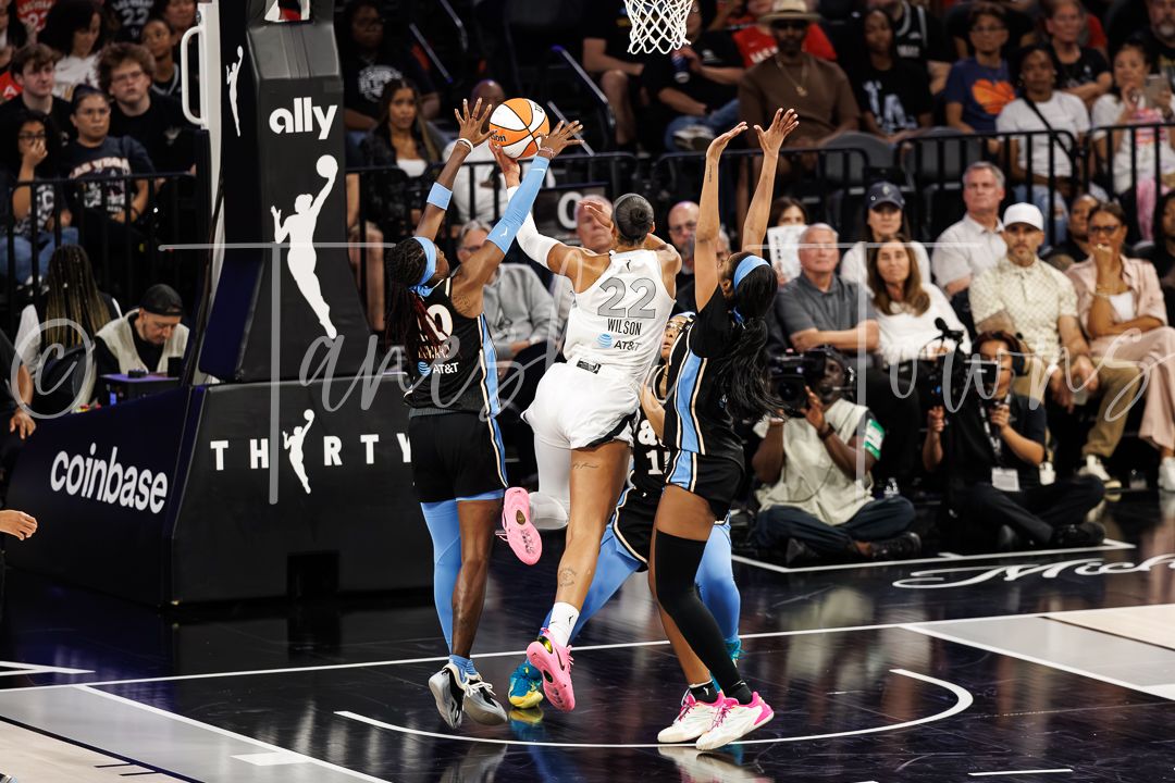 WNBA players compete for the ball during an intense game, with fans watching in the background.