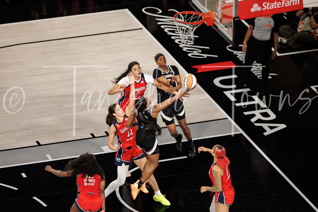 Aerial view of a WNBA basketball game with players driving to the hoop during an intense play.