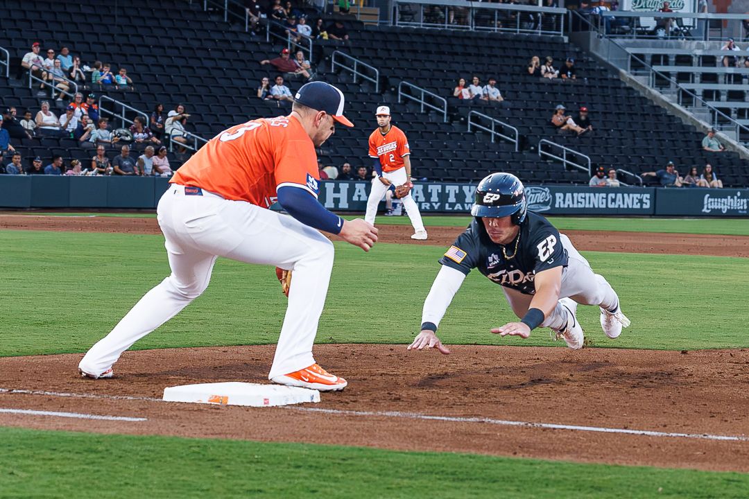 Baseball player diving to first base while fielder stretches to catch the ball during a college game.