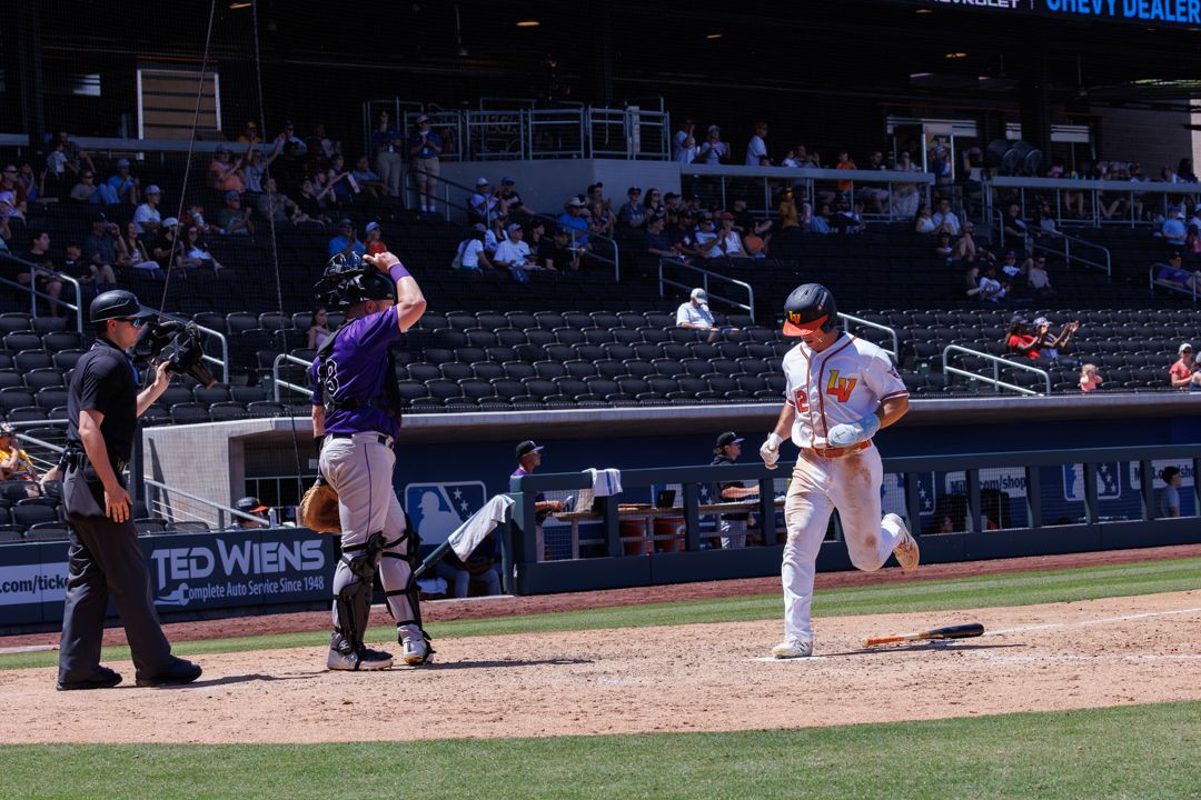 Baseball player scores a run at home plate as catcher and umpire watch during a college baseball game.
