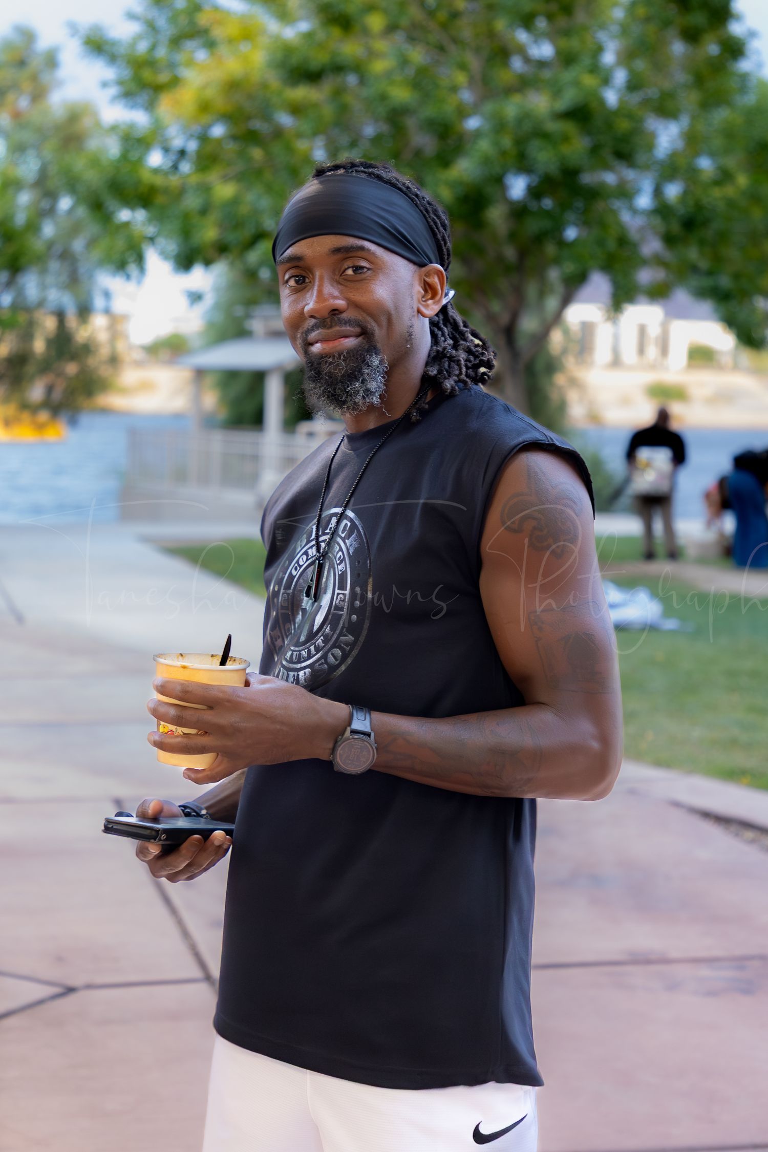 Person in black sleeveless shirt holding food outdoors on a sunny day.