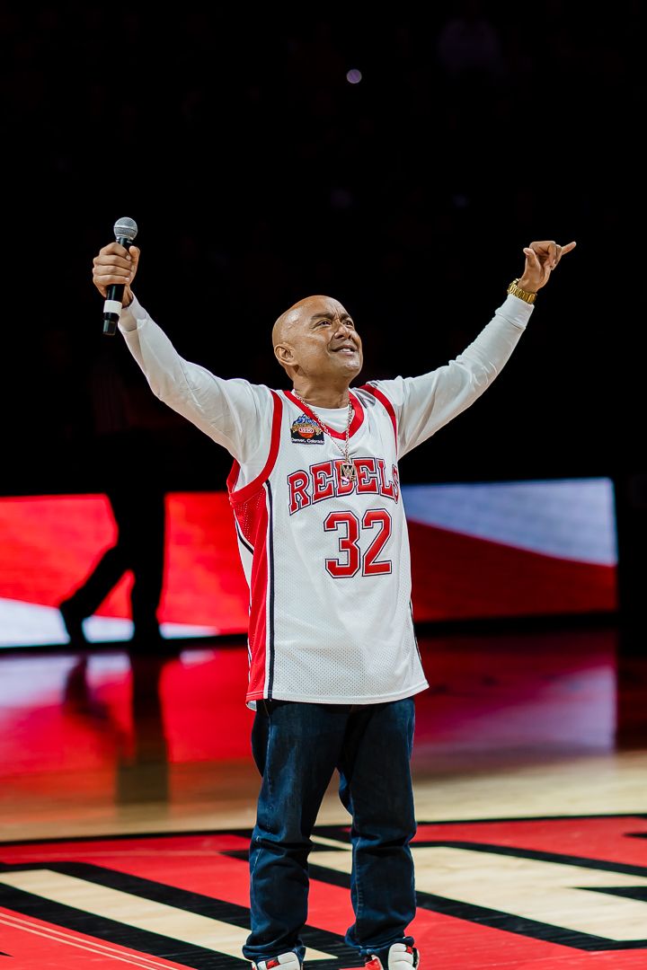 A performer in white jersey and dark pants raises their arms during a basketball game halftime show.
