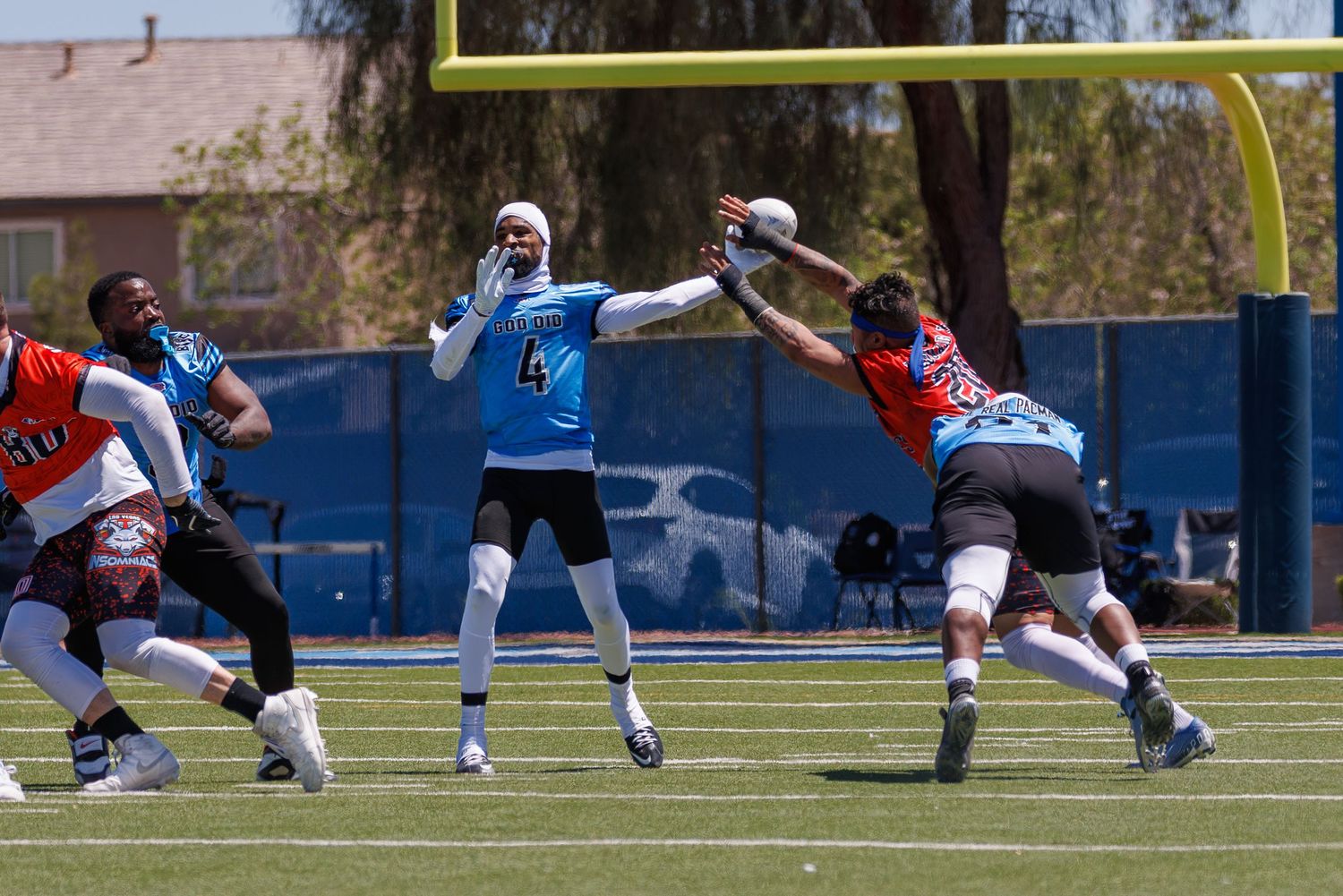 Players compete in a flag football game on a sunny blue field, with a quarterback throwing a pass under pressure.