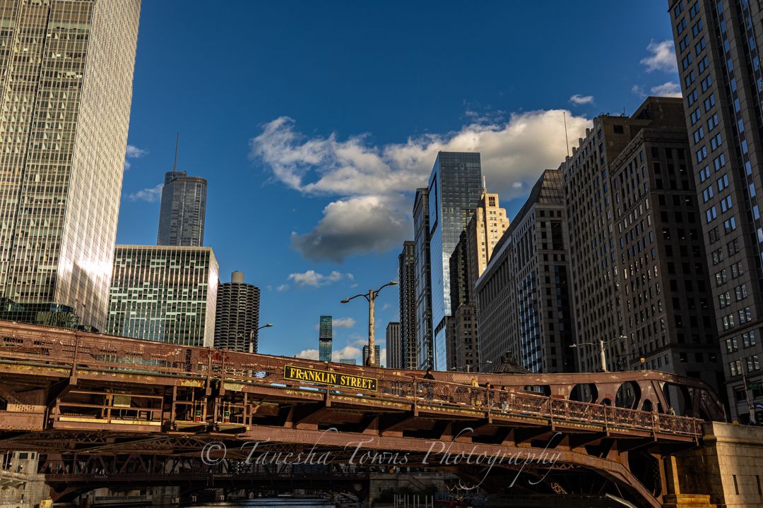 View of Chicago's iconic DuSable Bridge and downtown skyscrapers against a bright blue sky with white clouds.