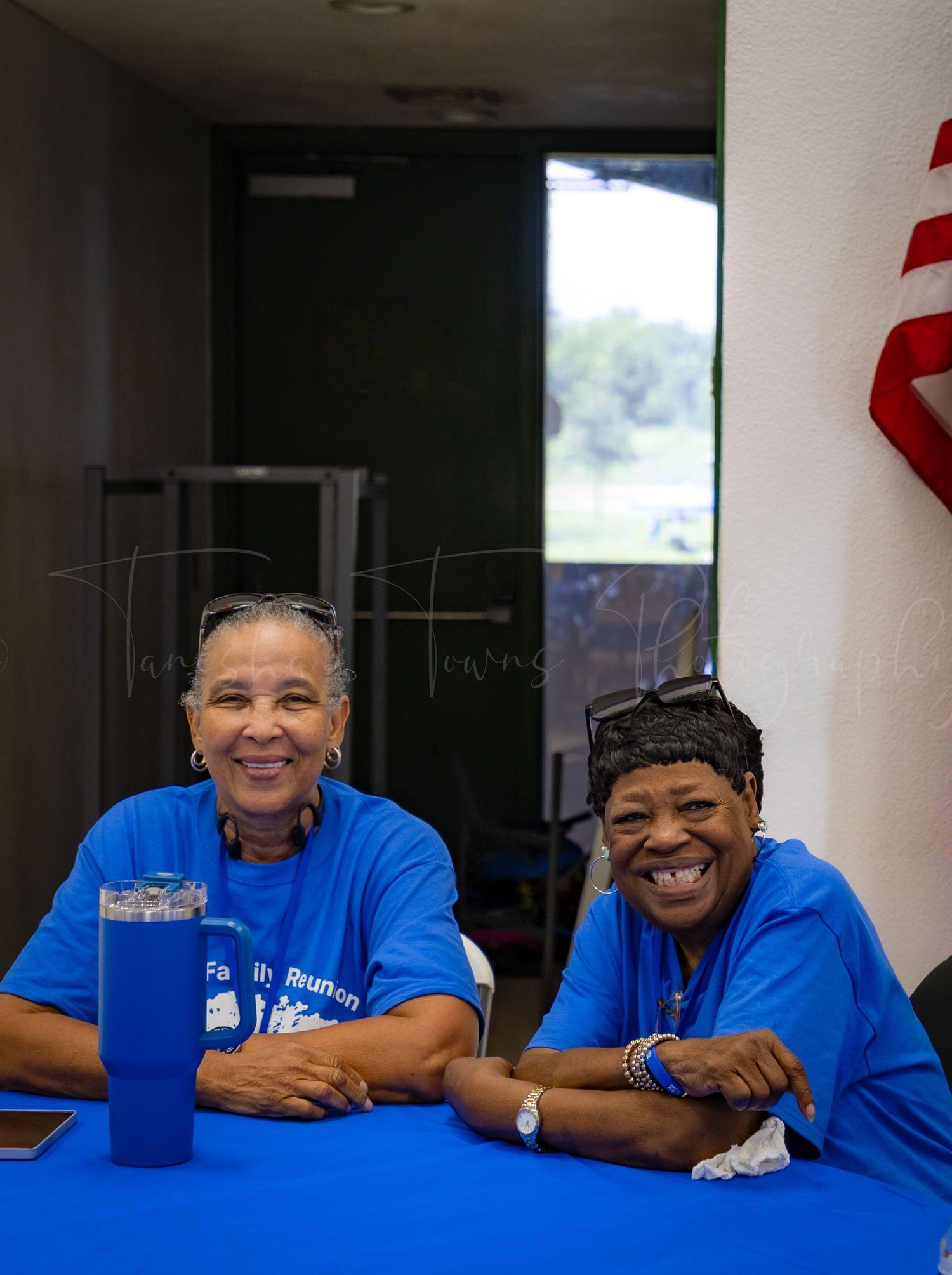 People in bright blue shirts smile while sitting at a table indoors.