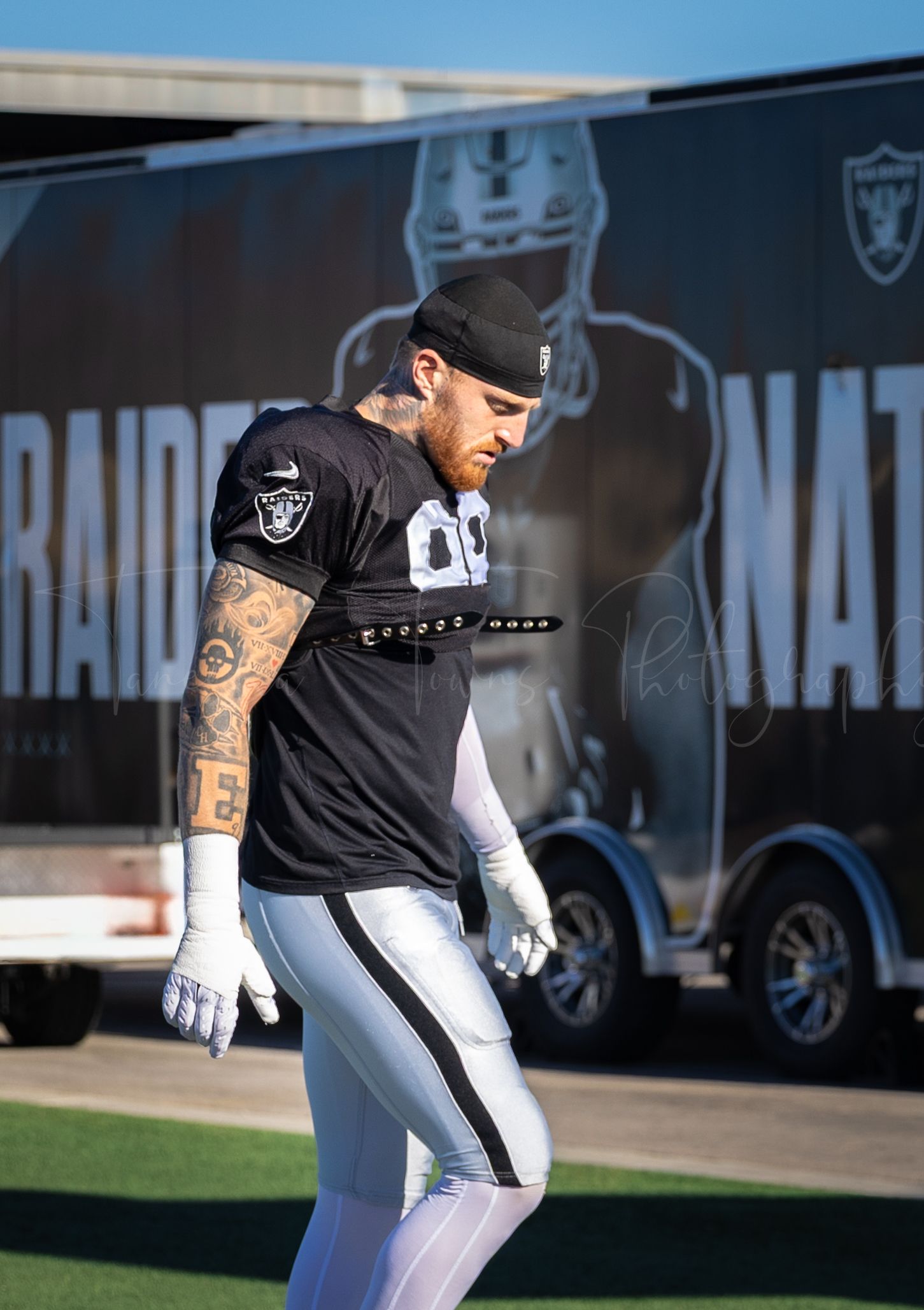 Raiders player in black jersey walks past team trailer during practice session.