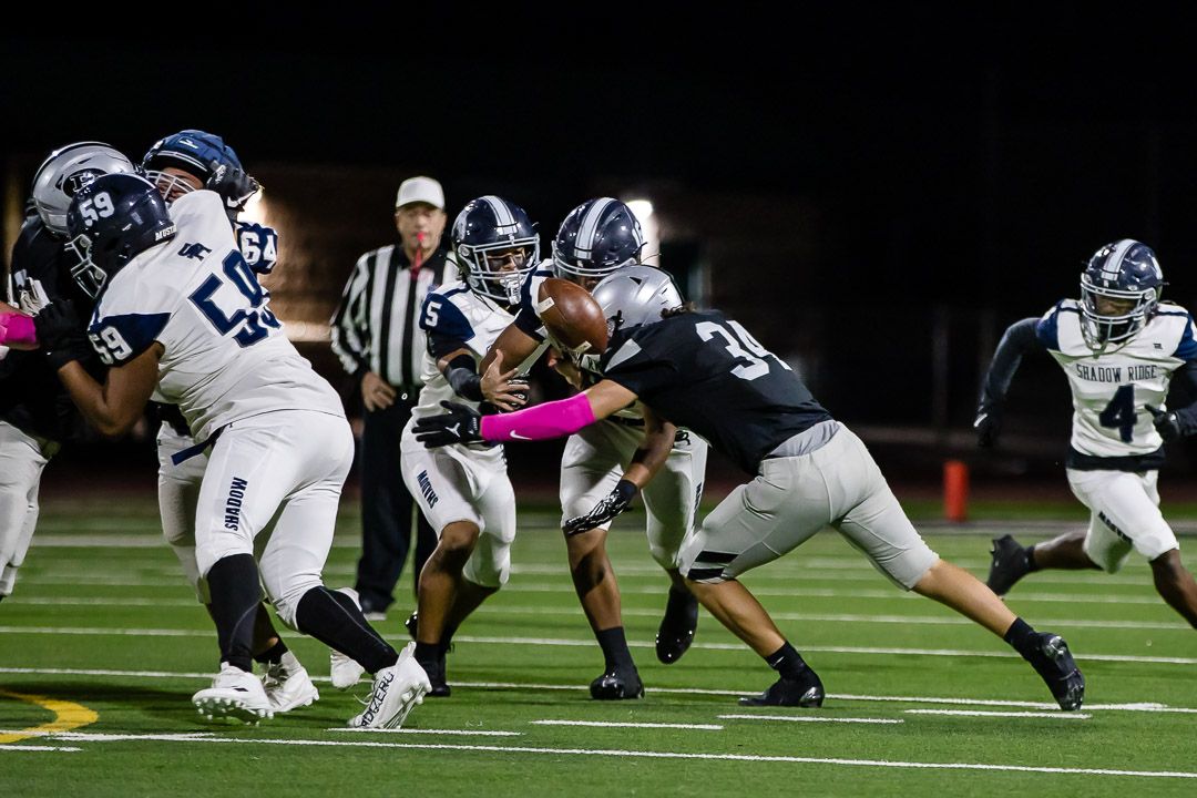 Football players scramble for possession during an intense ground play under stadium lights.
