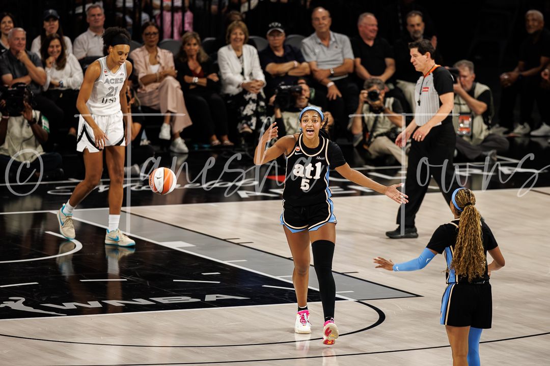 WNBA players compete on the court during a professional basketball game, with one player in a black uniform gesturing.
