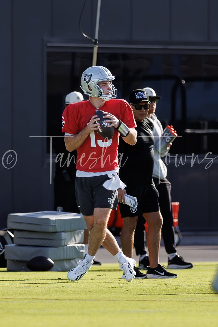 Las Vegas Raiders quarterback in red jersey and helmet prepares to throw during NFL practice session on field.