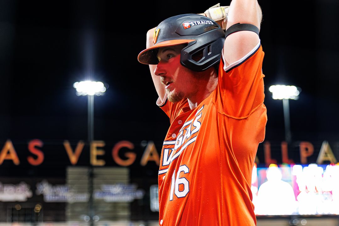 Baseball player in orange Las Vegas uniform adjusts helmet before batting.