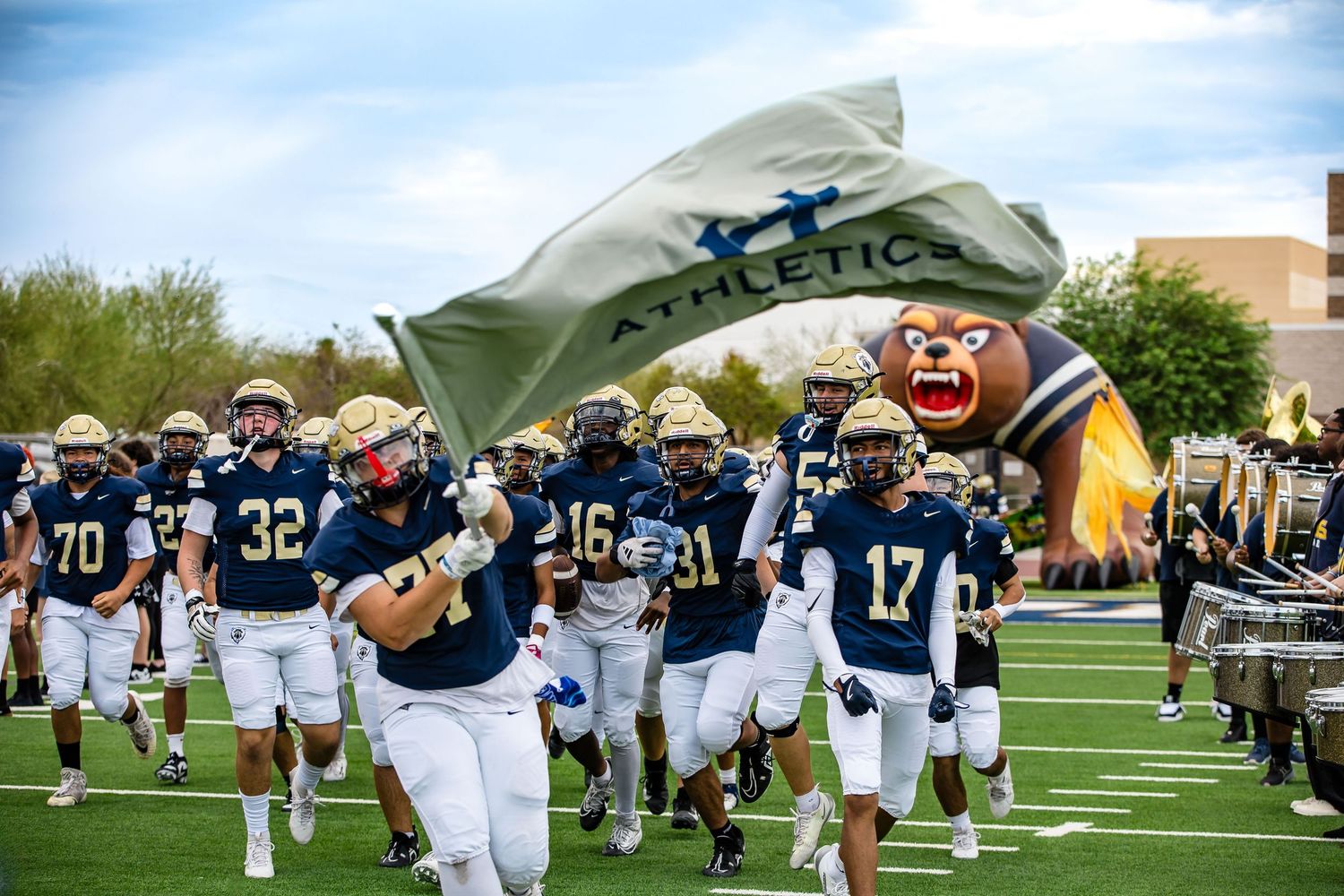 Football players running onto field carrying team flags during pre-game entrance.