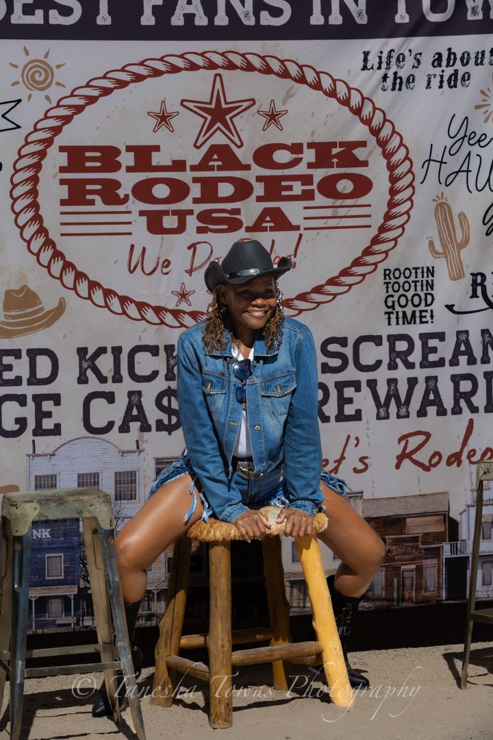 Denim-clad figures sit on yellow barrels against a western-themed backdrop with rodeo signage.