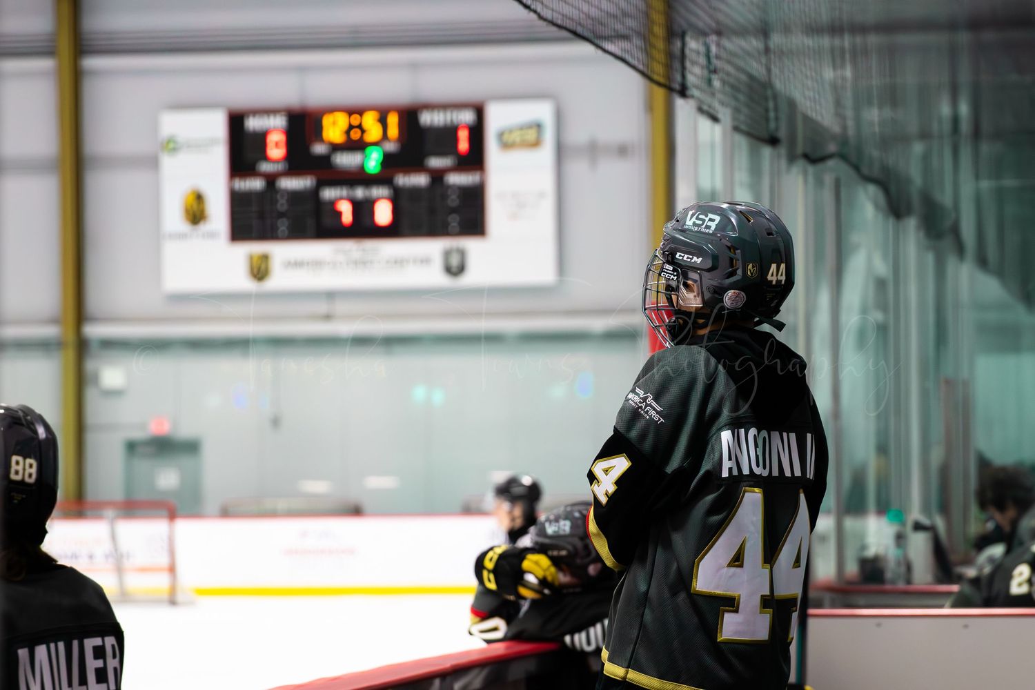 Hockey player in dark jersey watches scoreboard showing time remaining in period.
