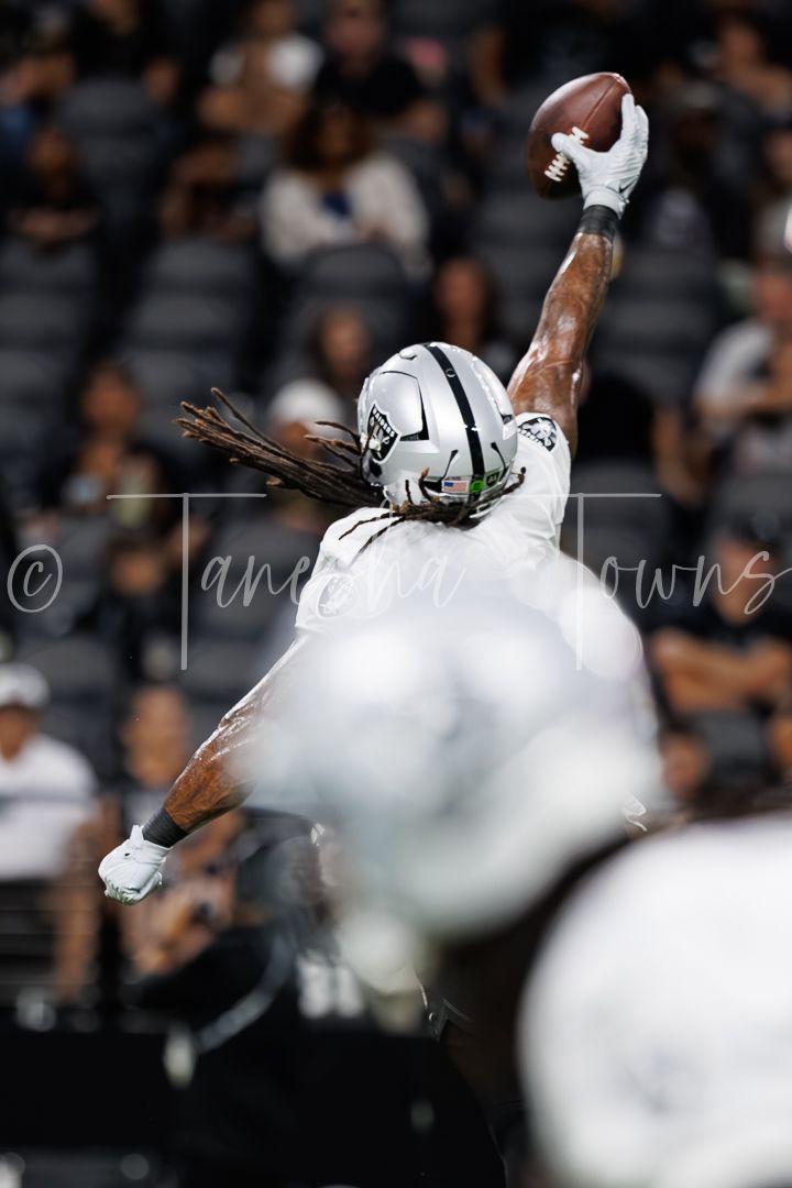 Raiders player extends one arm high to make a spectacular one-handed catch attempt during an indoor NFL game.