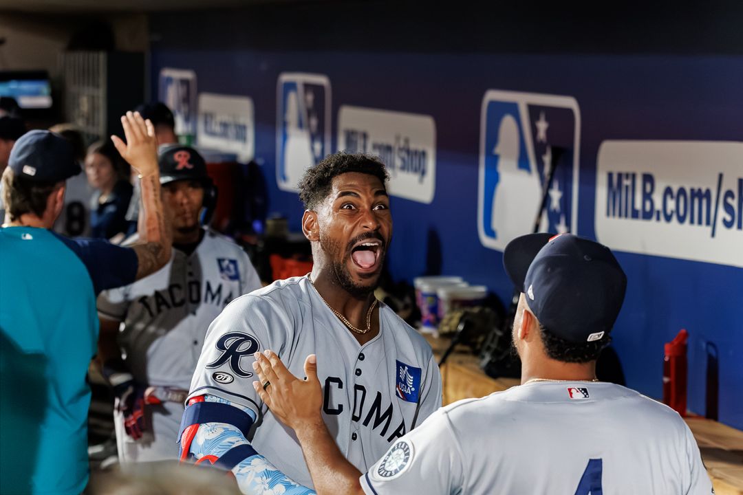 A Minor League Baseball player celebrates enthusiastically with teammates in the dugout during a game.