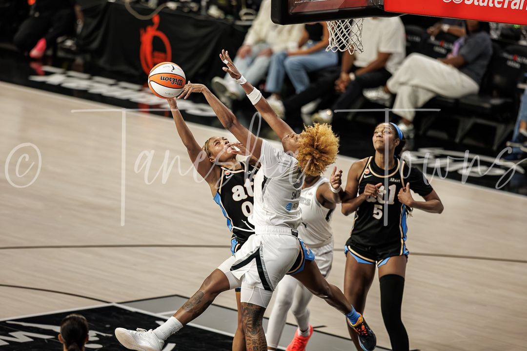 WNBA players compete for a layup during an intense basketball game, with defenders reaching to block the shot.