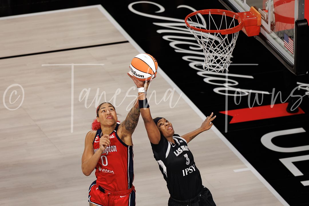 Two WNBA players compete for a layup near the basket during a professional women's basketball game.