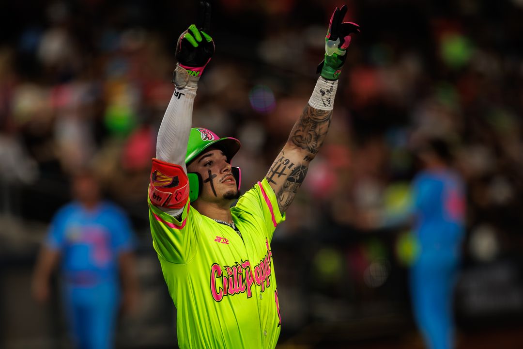 Baseball player in neon green uniform celebrates with arms raised after a hit during a night game.