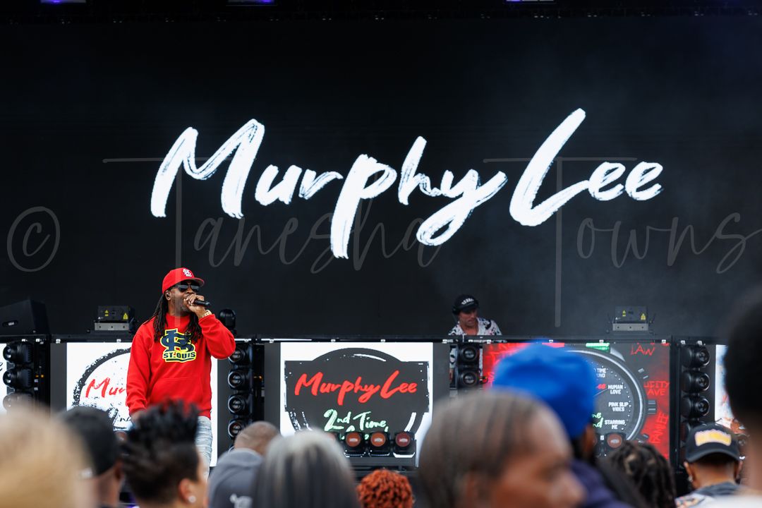 Murphy Lee performs on stage at an outdoor festival with his name displayed on large backdrop signage.