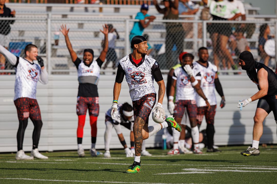 Flag football players celebrate on a stadium field wearing maroon and white jerseys during an outdoor game.