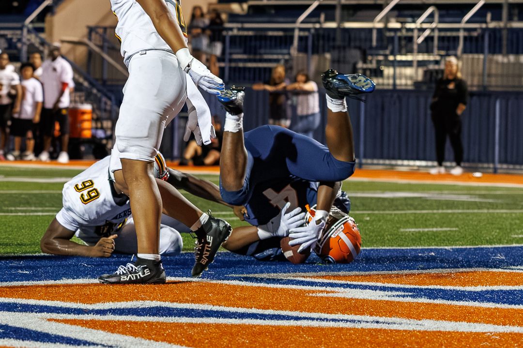 Football players collide in end zone during intense college game on blue and orange field.