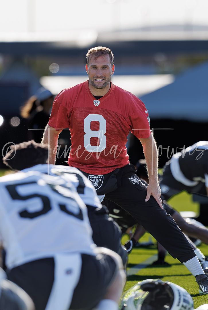 NFL player wearing number 8 red jersey smiles during Raiders football practice on outdoor field.