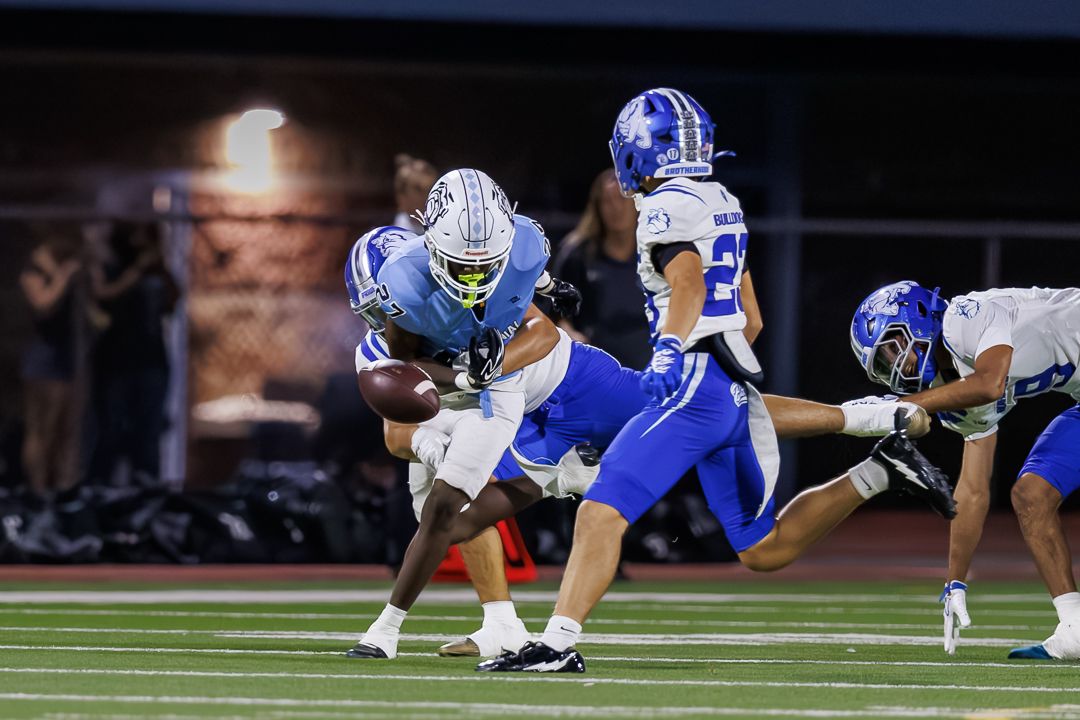 Football player in light blue jersey carries the ball during a nighttime high school football game.