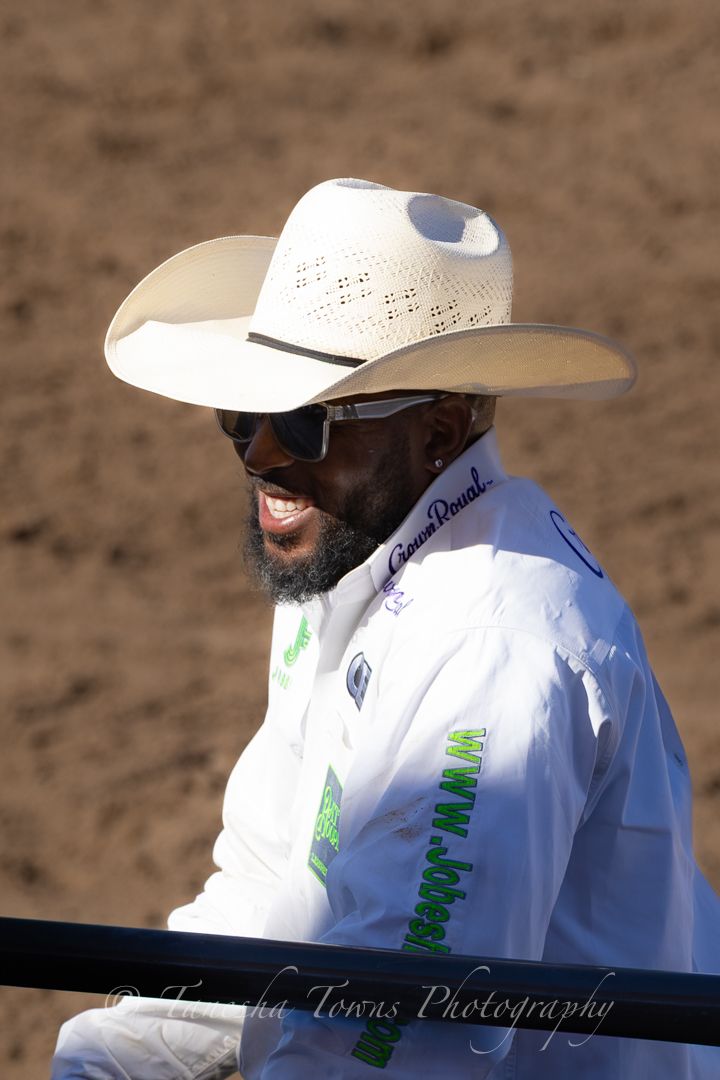 Spectators in white cowboy hats sit watching a rodeo event in bright sunlight.