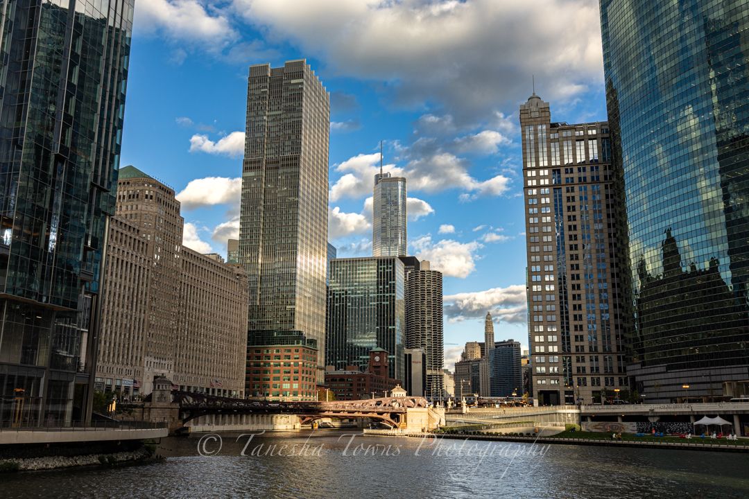 Panoramic cityscape of modern glass skyscrapers along Chicago River with dramatic clouds and blue sky.