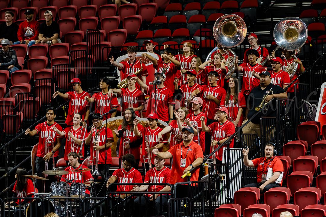 Marching band performs in red uniforms from stadium seating section.