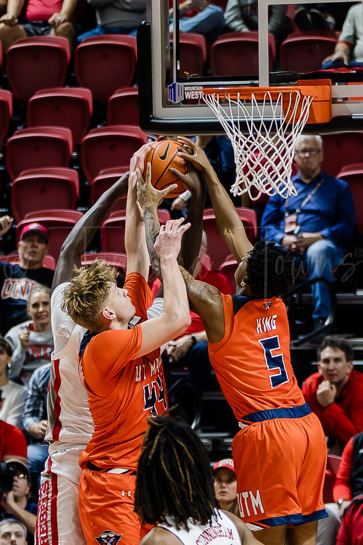 Basketball players from both teams fight for position under the hoop during a rebound attempt.