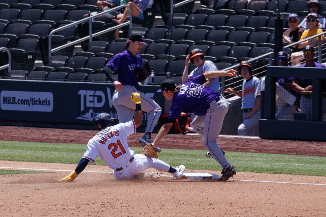 Baseball player slides into third base as fielder attempts tag during MLB game in sunny stadium.