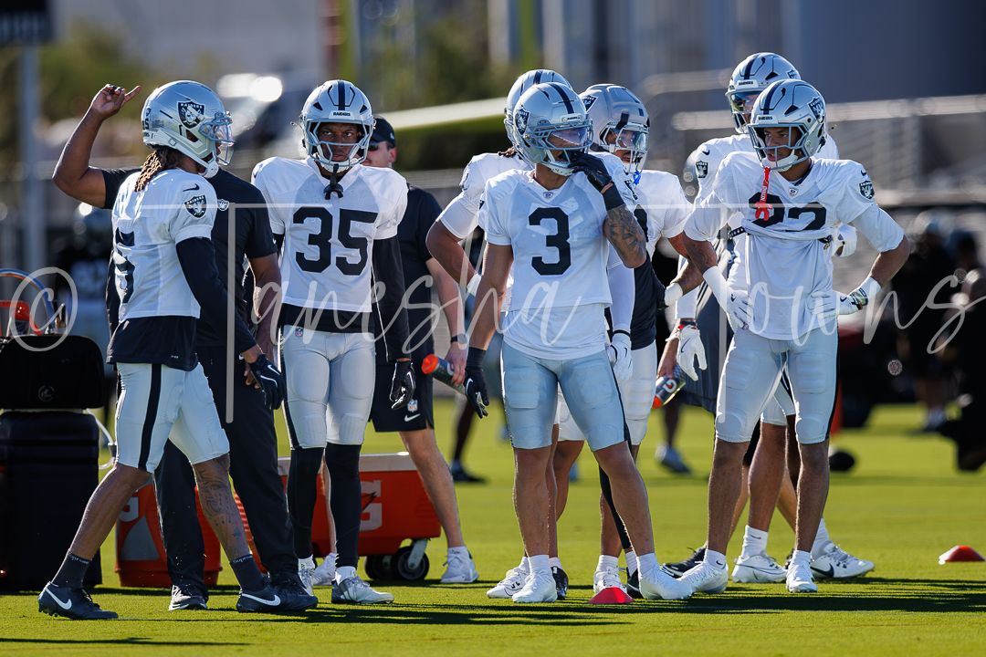 NFL players in white and navy uniforms huddle together during an outdoor training camp practice session.