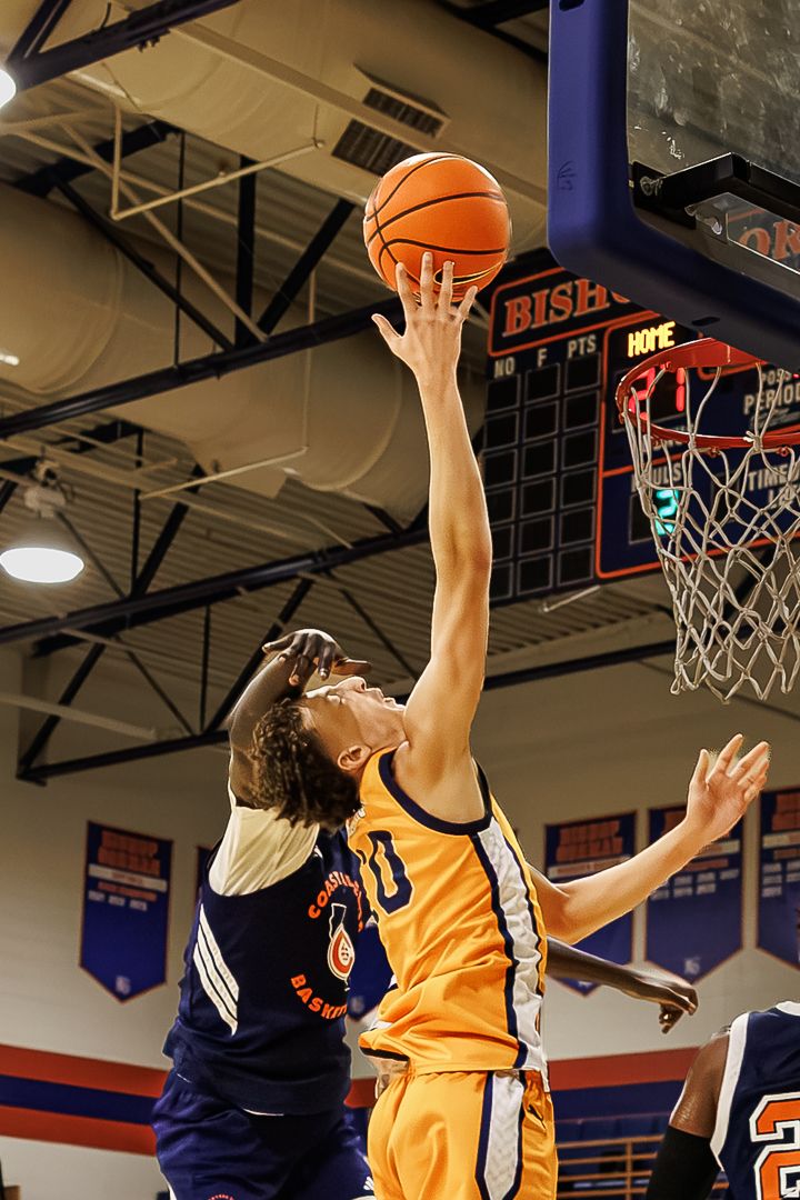 Two basketball players compete for a layup shot near the hoop during an indoor high school basketball game.