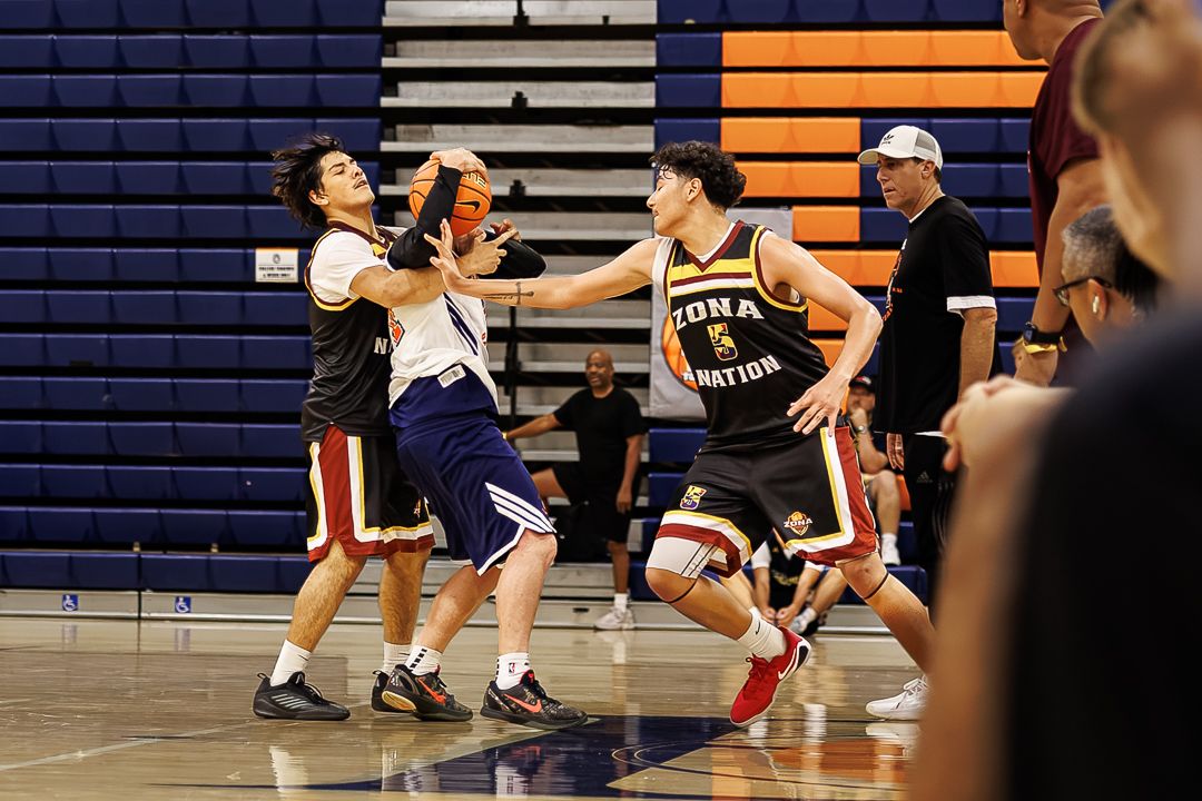 Basketball players in Gila Nation uniforms compete during an indoor game with spectators watching courtside.