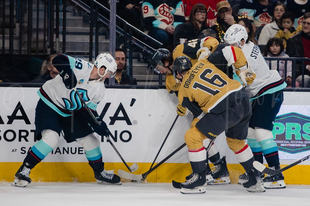 Hockey players from opposing teams fight for puck control along the boards during NHL game.