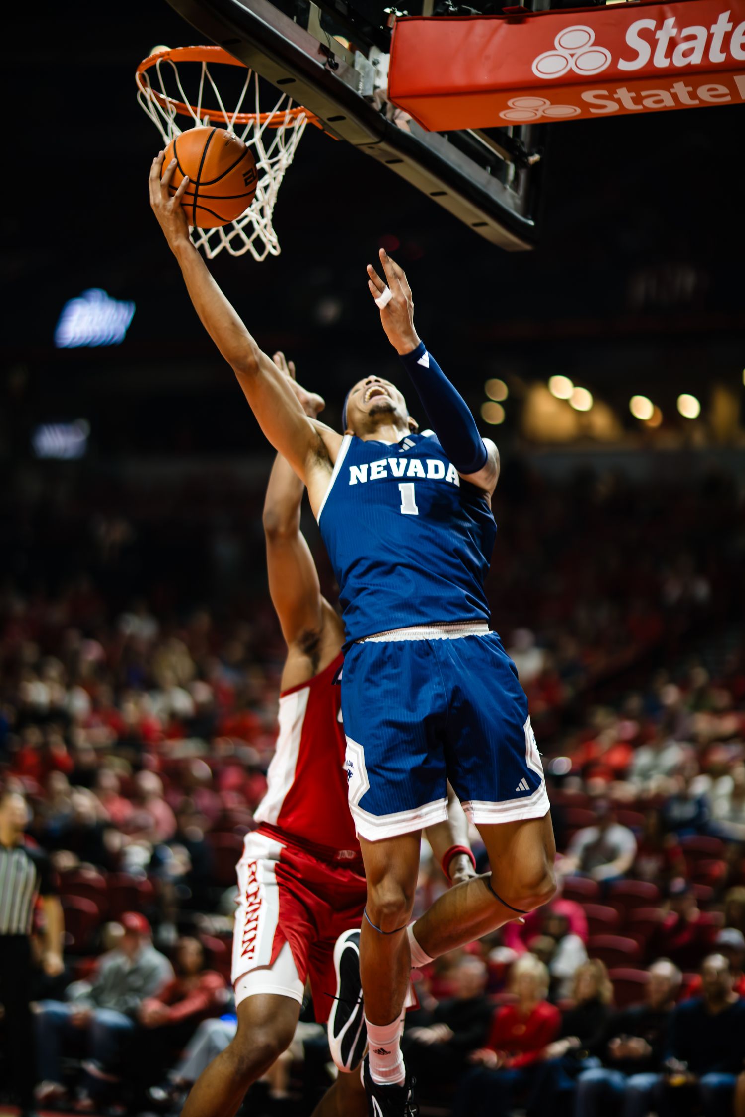 Nevada Wolf Pack player #1 drives to the basket for a layup during a college basketball game in a packed arena.
