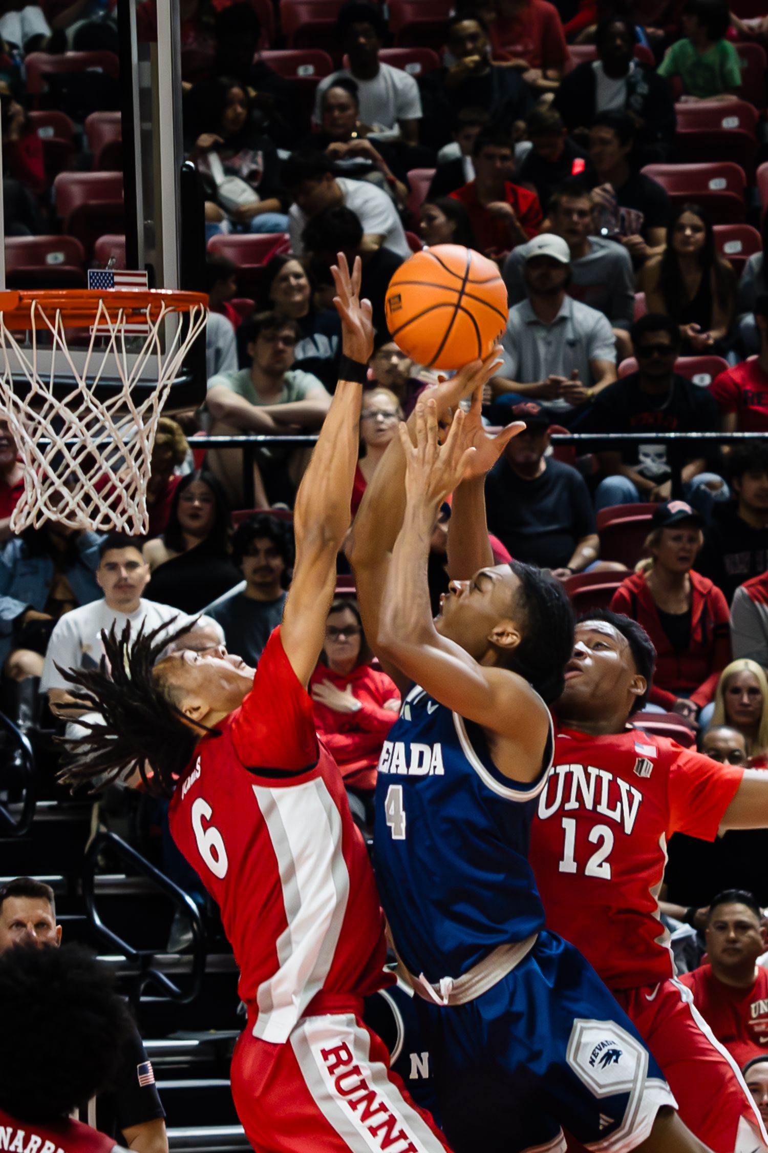 UNLV Runnin Rebels players #6 and #12 contest a shot against Nevada Wolf Pack #4 in a packed arena.