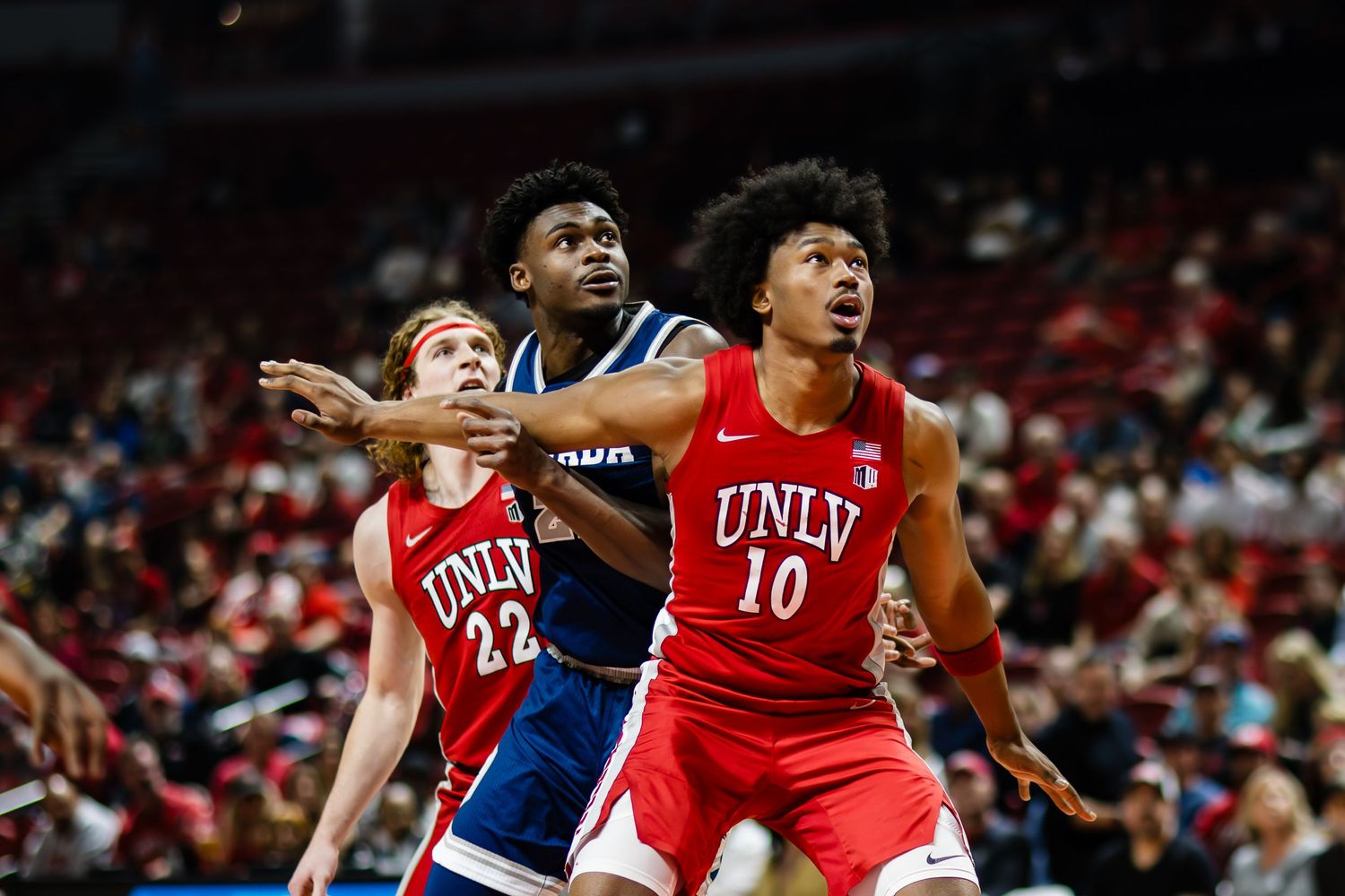 UNLV basketball players #10 and #22 box out during a college basketball game in red uniforms.