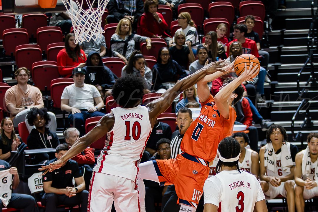 Basketball players from opposing teams in orange and white uniforms battle for possession during an intense game.
