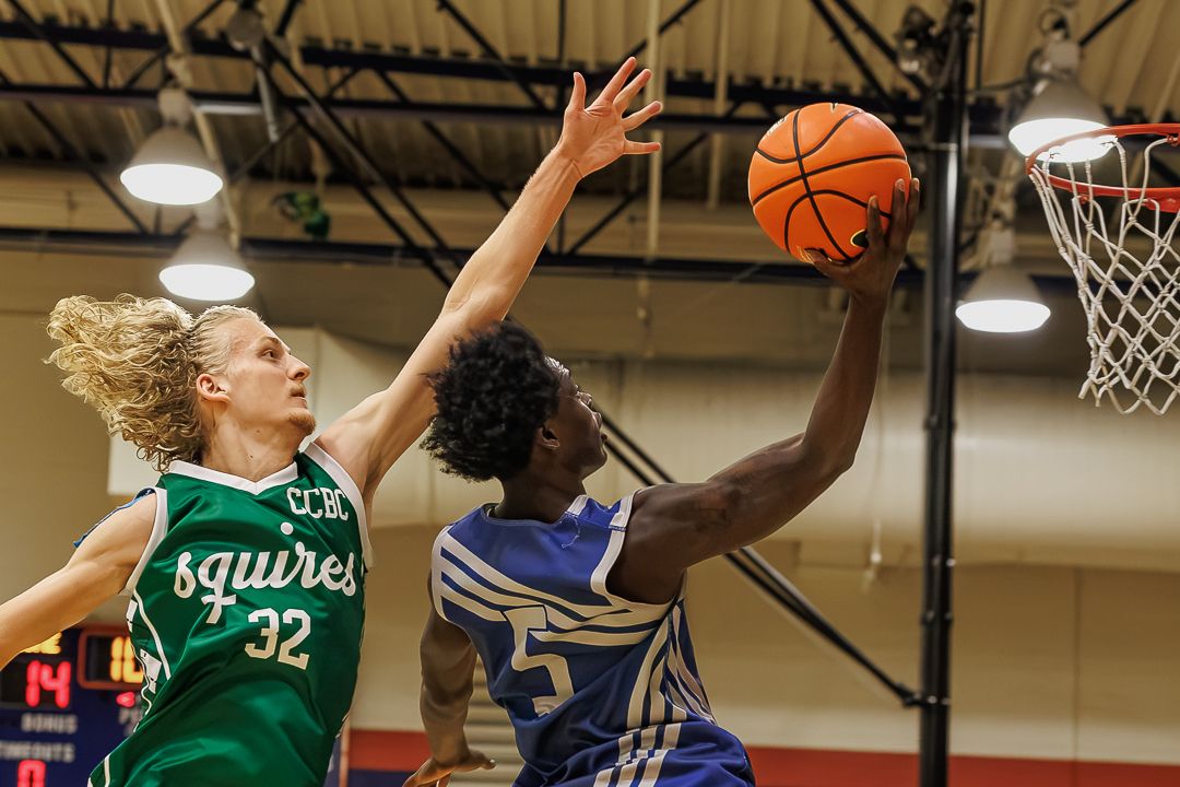 A blue-uniformed basketball player attempts a layup while defended by a green Squires player wearing number 32.