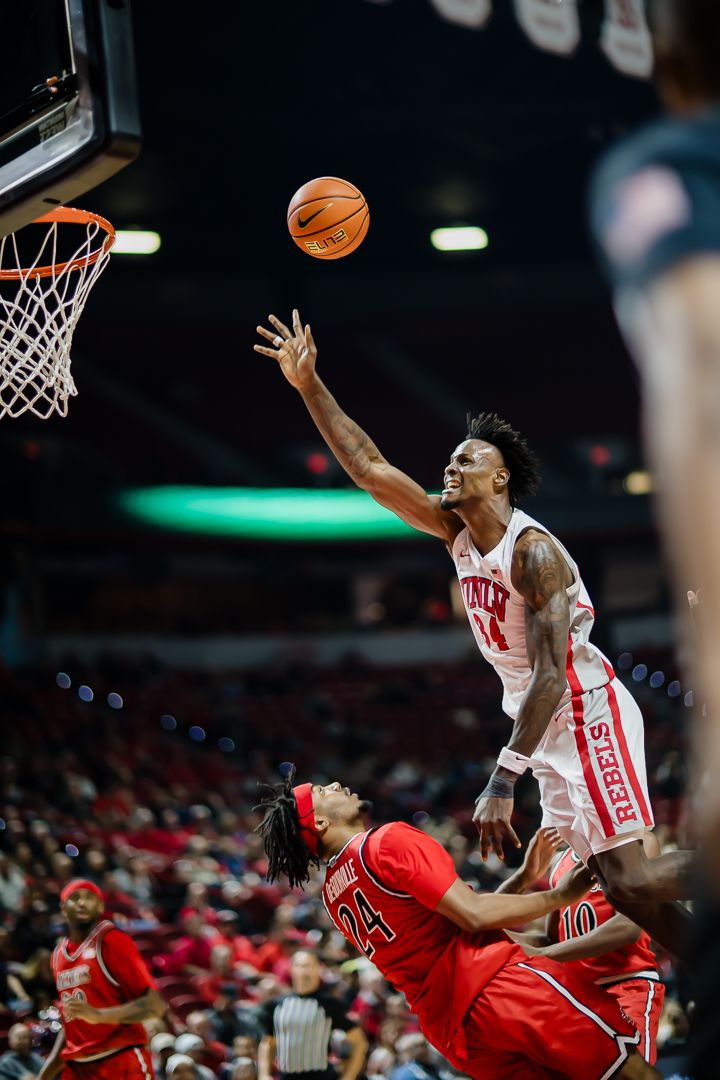 Basketball players leap and collide during an intense game between teams in red and white uniforms.