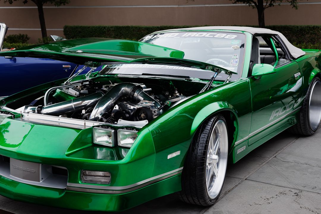 Bright green custom Chevrolet Camaro with open hood showcasing turbocharged engine at outdoor car show.