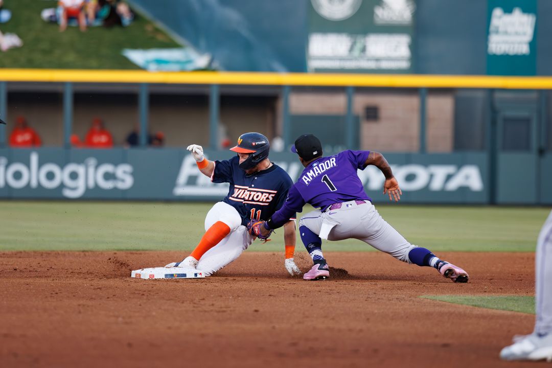 Baseball player slides into second base as infielder in purple uniform attempts tag.