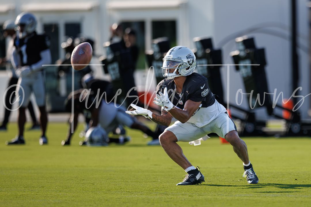 Raiders player reaches to catch a football during an NFL training camp practice session.