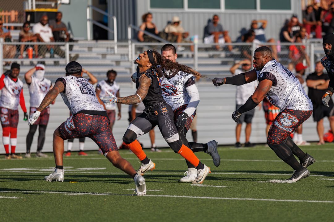 Football players in orange and maroon uniforms compete in an intense blocking play on a stadium field.