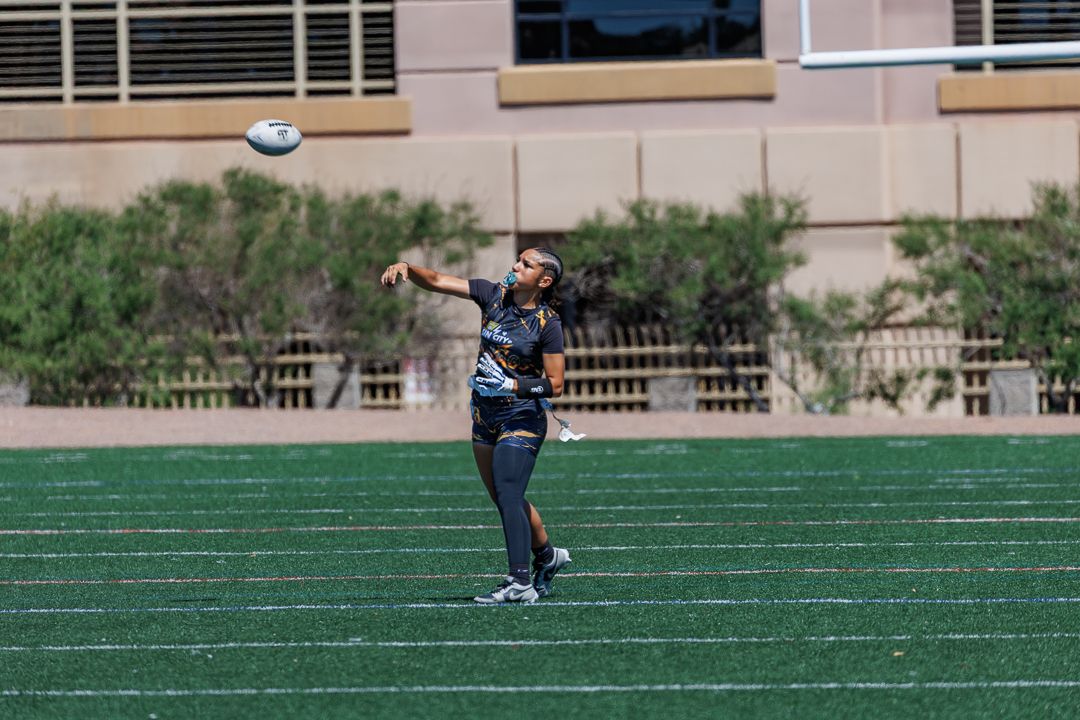 Rugby player throwing a ball on a green turf field during an outdoor practice session in sunny weather.