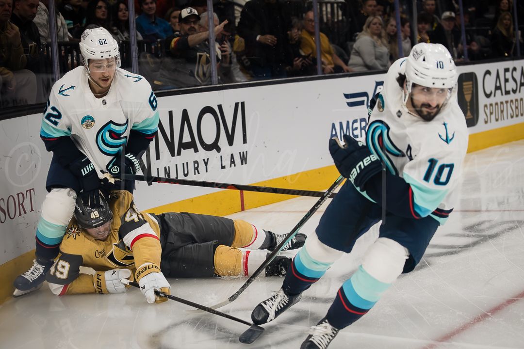Hockey players from opposing teams battle for the puck along the boards during an NHL game.
