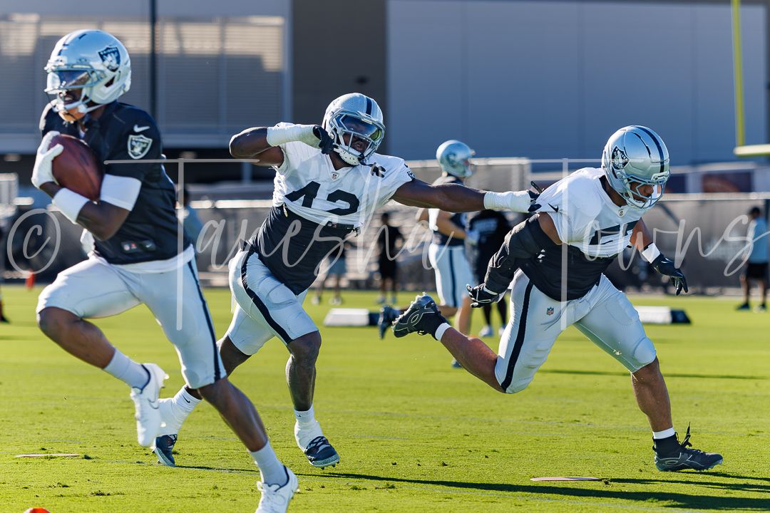 Raiders players run drills during NFL training camp practice on a sunny day outdoors.