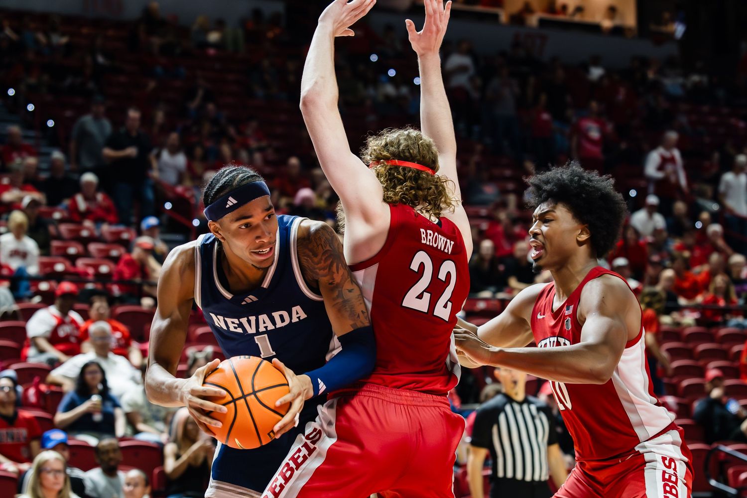 Nevada Wolf Pack player drives to the basket against two Fresno State Bulldogs defenders during a college basketball game.